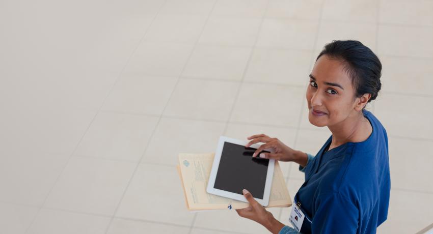 smiling nurse looking at viewer, holding tablet device