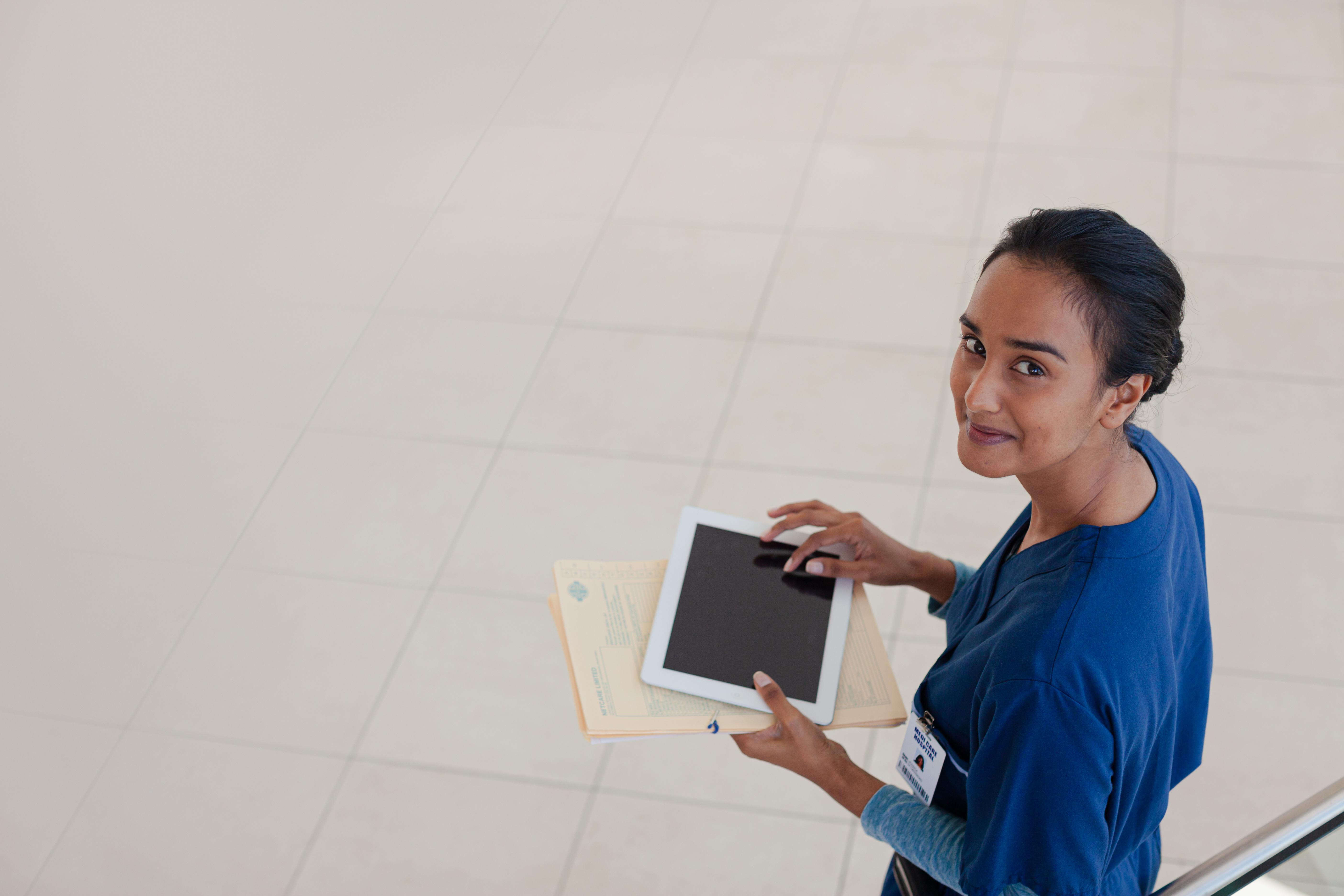 smiling nurse looking at viewer, holding tablet device